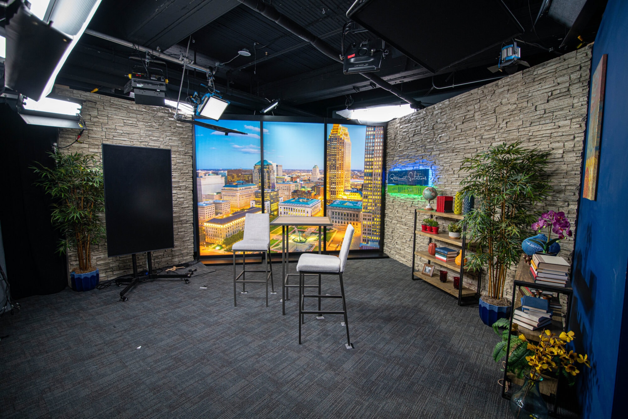 Cityscape backdrop with studio seating and decorative plants in a professional video production studio.